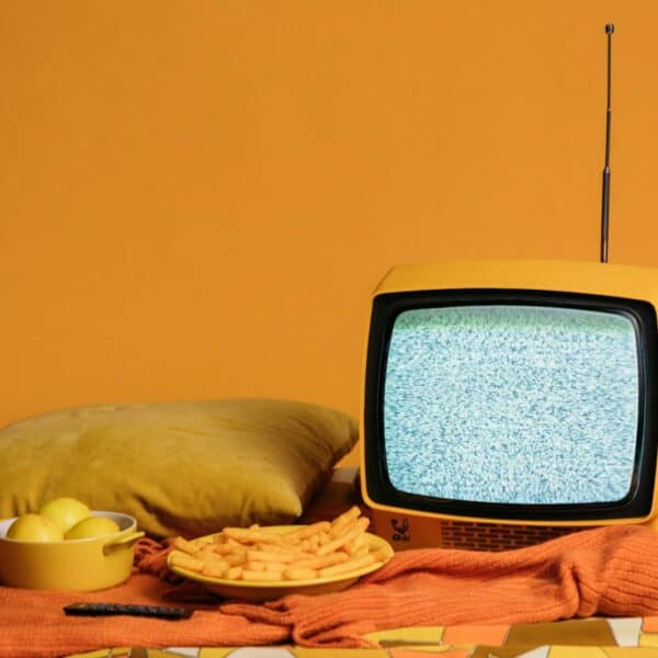 A vintage yellow TV with static, surrounded by fries, apples, and a cozy pillow setup.